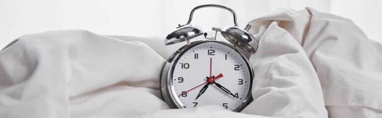 האם באמת אפשר להשלים שעות שינה בסוף השבוע? שעון במיטה