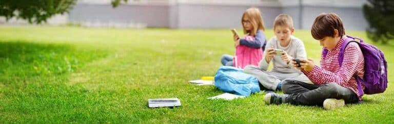 קרינה אלקטרו מגנטית בילדים - בתמונה ילדים יושבים על הדשא ושקועים בסמארטפונים שלהם