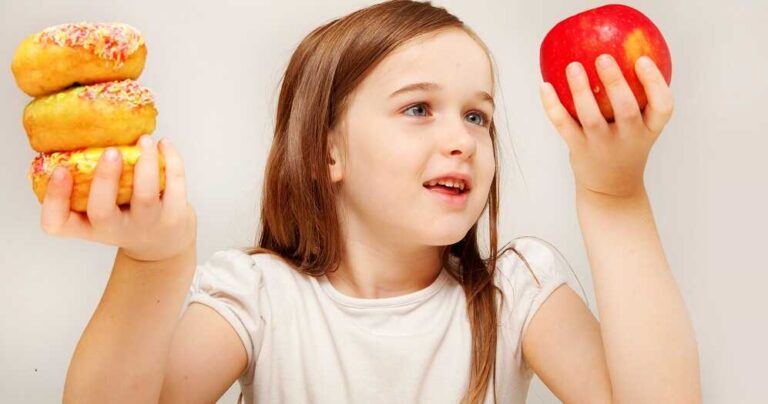 גמילת ילדים ממזון תעשייתי מזיק - בתמונה ילדה המתלבטת עם לאכול תפוח או דונאטס