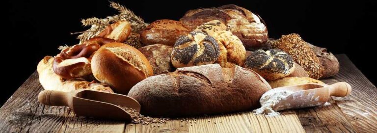 איך לבחור לחם בריא בחנות טבע? - בתמונה מגוון לחמים מונחים על משטח עץ